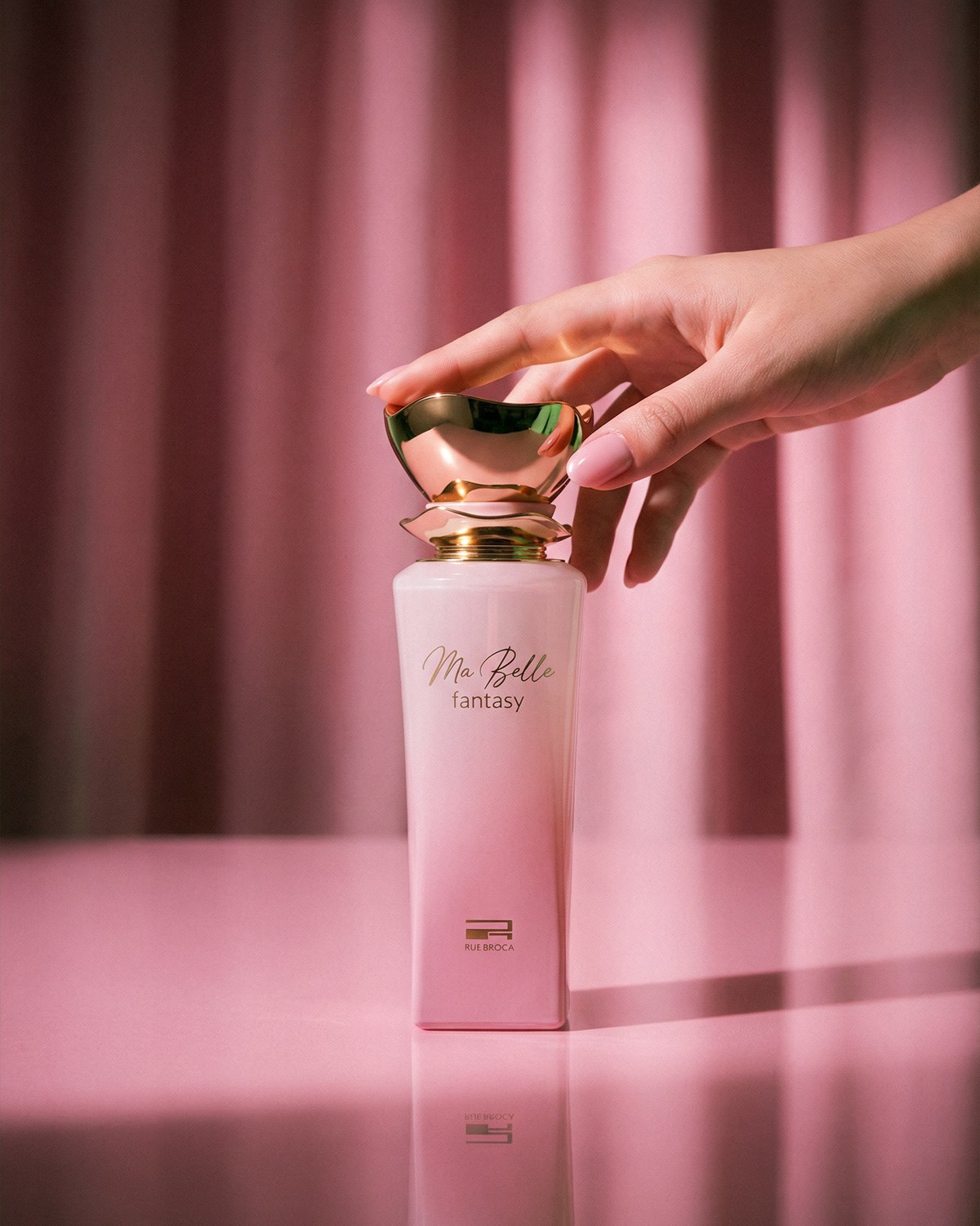 A hand holding a pink Rue Broca perfume bottle against rose-coloured curtains — AI perfume imagery by The Media Lab.